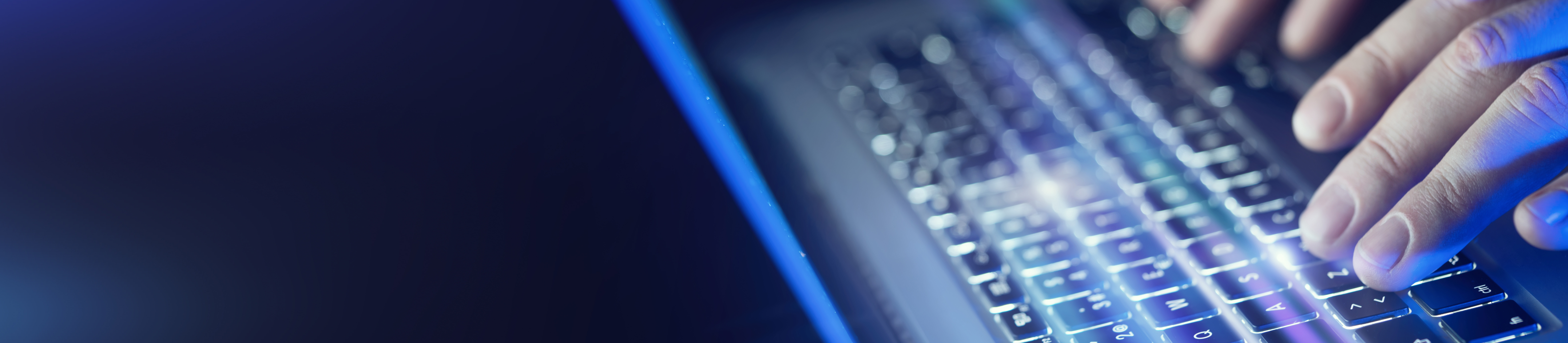 Close up of hands typing on a blue blacklit laptop keyboard