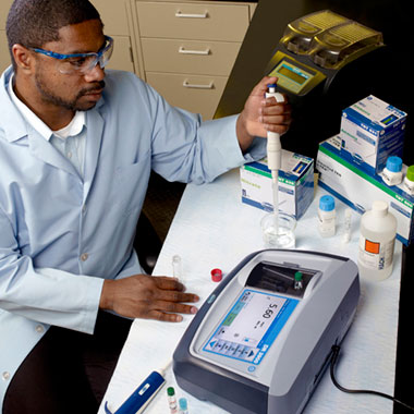 Lab technician performing water quality testing with Hach benchtop spectrophotometer.